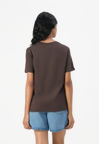 Brahka kratki rokav t-shirt z okroglo ovratnikom, prikazan zadaj, v kombinaciji z modrimi jeans kratkimi hlačami. Gladka tekstura, sproščen kroj.