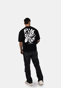 Czarna koszulka z krótkim rękawem z białym nadrukiem "RISE & SHINE" na plecach, połączona z ciemnoniebieskimi dżinsami i białymi trampkami.