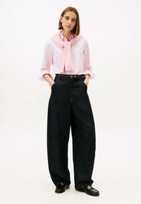 Light pink striped shirt worn with a pastel pink sweater tied at the neck, paired with high-waisted dark denim wide-leg trousers and black loafers.
