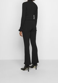 Ensemble de détente noir à côtes comprenant un col roulé ajusté et un pantalon évasé. Le pull a des poignets à volants ; le pantalon est à longueur de cheville avec une coupe ajustée.