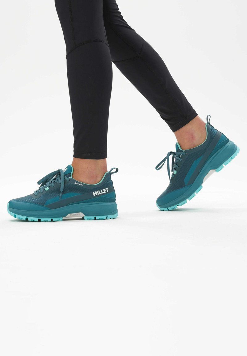 Türkise Outdoorschuhe mit strukturiertem Material, gepolsterten Sohlen und einem robusten Grip-Muster. Mit blauen Akzenten und dem "Millet"-Logo.