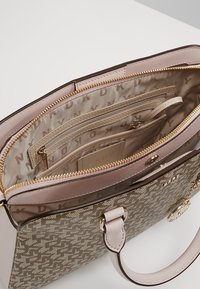 Sac à main beige à motif avec poignées rose clair, fermeture éclair dorée, poche intérieure zippée, emplacement pour cartes et doublure avec logo DKNY.