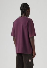Bordeaux oversized t-shirt met korte mouwen en een ronde hals, gemaakt van katoen. Heeft een subtiele gradient die naar de zoom vervaagt.