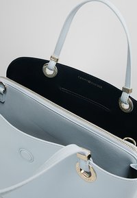 Jasnoniebieska skórzana torebka Tommy Hilfiger z podwójnymi uchwytami, zamkiem błyskawicznym oraz złotymi metalowymi detalami w kształcie pierścieni.