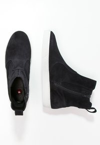 Bottes de cheville en suède noir avec une semelle en caoutchouc blanc, dotées d'une fermeture éclair sur le côté et d'une finition lisse, conçues pour un enfilage facile.