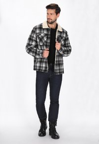 Czarna i biała kurtka w kratę z kołnierzem Sherpa, z dwiema kieszeniami na piersi, w połączeniu z ciemnymi dżinsami i czarnymi szytymi butami.