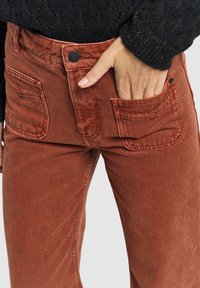 Rustkleurige corduroy broek met twee achterzakken, voorzien van een textuurafwerking en een metalen knoopsluiting bij de taille.