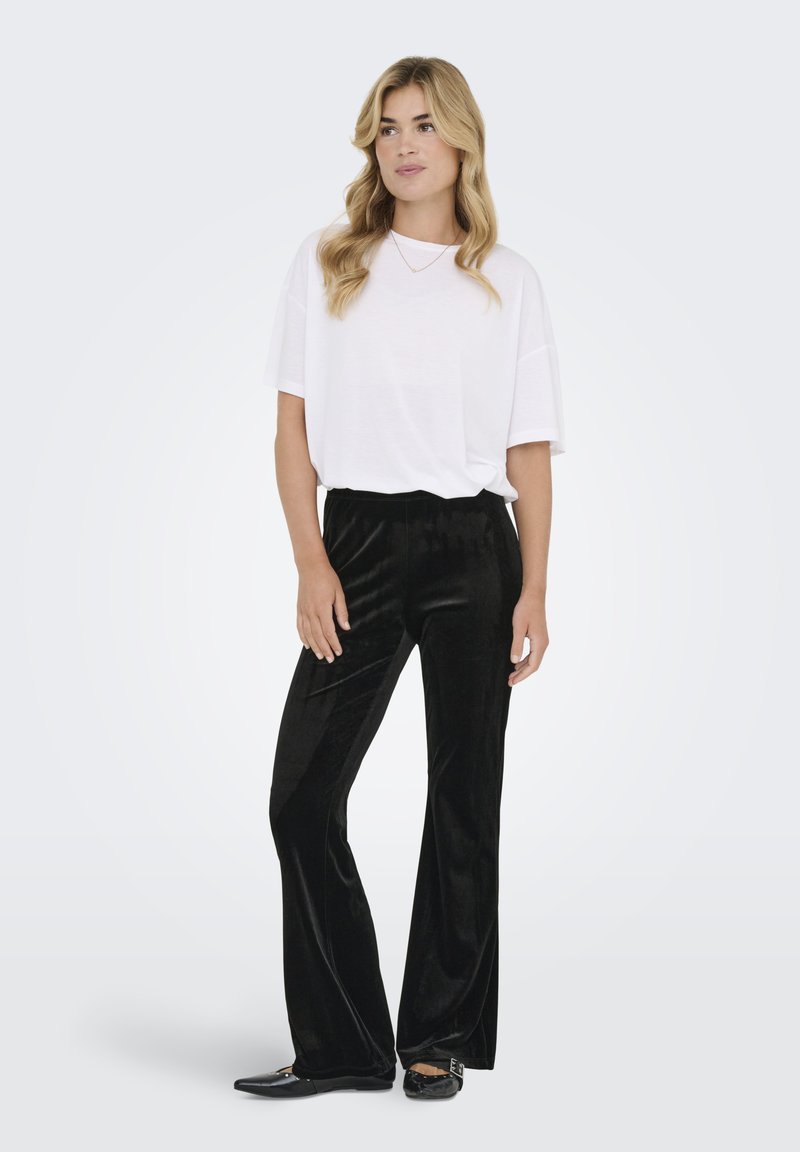 Maglietta bianca oversize abbinata a pantaloni neri in velluto a gamba larga. I pantaloni hanno una texture liscia, mentre le scarpe sono ballerine nere lucide.