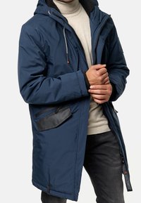 Parka bleu marine avec une capuche texturée, des accents noirs, une fermeture éclair à l'avant et des détails de poches latérales. Elle comporte des poignets élastiques et une doublure chaude.