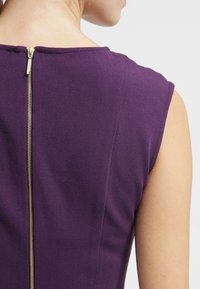 Robe sans manches de couleur pourpre avec une texture lisse, dotée d'une fermeture éclair dorée à l'arrière et d'un col rond classique.