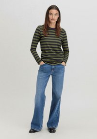 Gestreiftes Langarmoberteil mit olivgrünen und marineblauen Streifen, kombiniert mit blauen, weiten Jeans und schwarzen Schuhen. Glatter Stoff, lässige Passform.