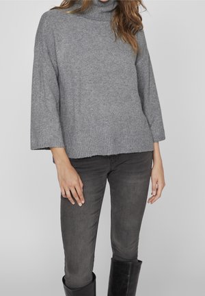 Grau gestrickter Rollkragenpullover mit lockerer Passform, weiten Ärmeln und einem gerippten Saum. Kombiniert mit dunklen Jeans und schwarzen kniehohen Stiefeln.