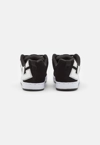 Black and white sneakers with a low-top design, featuring a suede upper, textured accents, and pronounced logo on the heel. White sole.