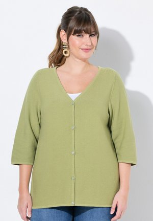Olijfgroene cardigan met V-hals, knoopsluiting en driekwart mouwen. Textuurstof met een relaxte pasvorm, gecombineerd met een witte top eronder.