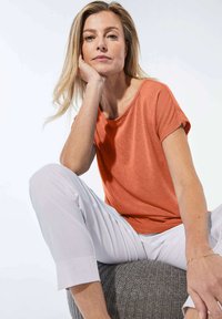 Losse oranje T-shirt van een zachte breisel, gecombineerd met witte cropped broek. Het shirt heeft een brede halslijn en korte mouwen.