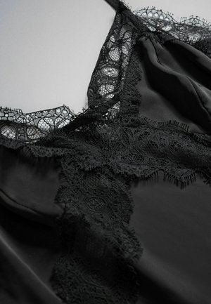 Černé saténové spodní prádlo s květinovou krajkou podél výstřihu a ramínek na rovinném světle šedém povrchu.