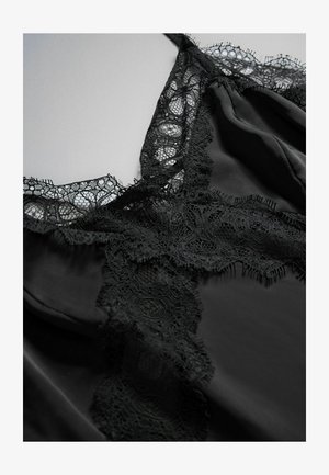 Lenjerie neagră din satin cu dantelă florală decorativă de-a lungul decolteului și bretelelor, așezată pe o suprafață plată de culoare gri deschis.