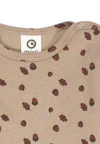 Tessuto ribbed beige con una stampa di foglie e ghiande sparse in rosso scuro e verde. Chiusura a scatto sulla spalla per una facile vestizione.