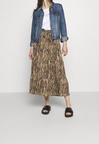 Ker skirt berlapis dengan corak haiwan coklat dan hitam, dipadankan dengan jaket denim dan selipar hitam. Menampilkan potongan santai dan reka bentuk kasual.