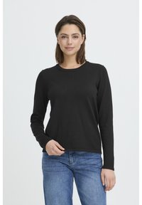 Haut noir à manches longues avec un col rond. Texture douce et lisse avec une coupe ajustée, associé à un jean en denim bleu clair.