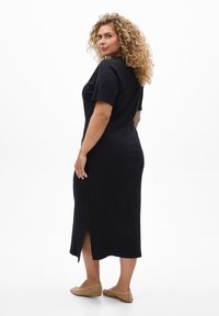 Vestido midi negro de canalé con mangas cortas y bordes en forma de ola, con una abertura lateral. Tejido ligero y ajustado, de longitud hasta el tobillo.