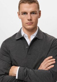 Polo de manga larga gris oscuro con cuello abotonado, que presenta un interior de cuello blanco y puños en capas. Textura suave, diseño informal.