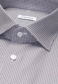 Gros plan sur le col d'une chemise à motifs avec des boutons blancs et une étiquette cousue indiquant "seidensticker".