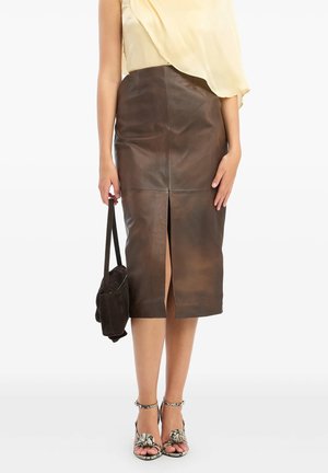 Donna con gonna midi in pelle marrone con spacco frontale, che tiene una borsa scura e indossa sandali con tacco e stampa di serpente.