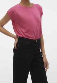 Maglietta rosa a maniche corte realizzata in un tessuto morbido, abbinata a jeans neri a vita alta. La maglietta presenta un collo rotondo e una vestibilità comoda.
