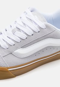 Szürke velúr sneaker fehér bőr díszítéssel, fehér fűzőkkel és gumi talppal. Perforációkkal és klasszikus oldalsávos dizájnnal rendelkezik.