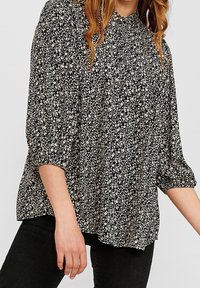 Blouse noire à motifs floraux avec manches trois-quarts, dotée d'un col froncé et de petits imprimés floraux blancs et beiges sur un tissu doux.