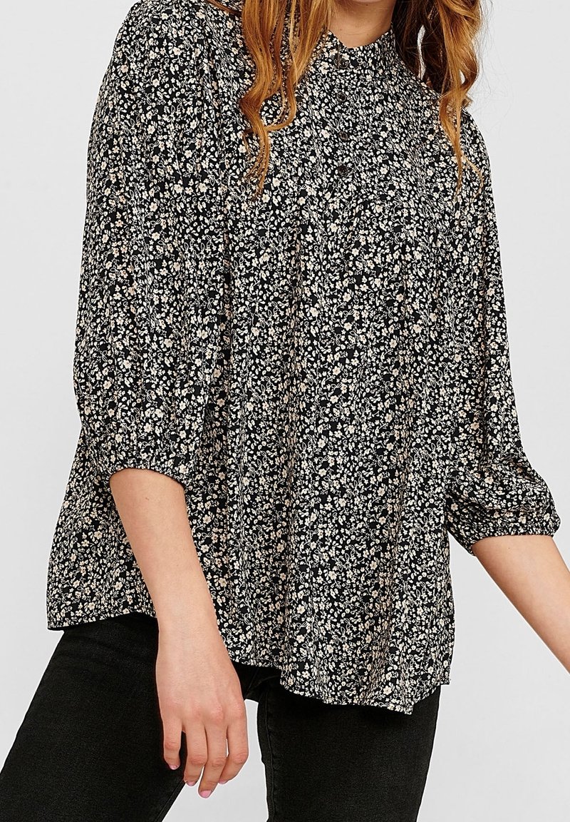 Blouse noire à motifs floraux avec manches trois-quarts, dotée d'un col froncé et de petits imprimés floraux blancs et beiges sur un tissu doux.