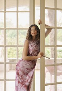 Roosa marmorimustriga kleit, millel on läikiv siluett; sile kangas, millel on peen sära; kantud, kui toetutakse klaasuste najale.