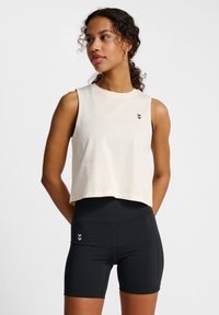 Cropped light beige sleeveless top with a round neckline and a small black logo, paired with form-fitting black shorts featuring side detailing.