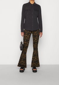 Zwarte denim shirt met twee borstzakken, gecombineerd met bruin en zwart luipaardprint flare broek en dikke zwarte platform sandalen.