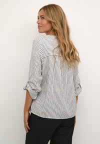 Blouse rayée avec des lignes blanches et navy, tissu doux, manches trois quarts, design ample avec un ourlet arrondi et une fente à l'arrière.