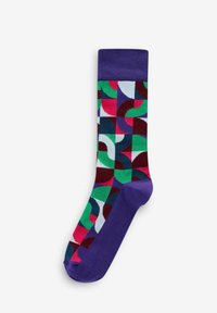 Chaussette en coton colorée avec des motifs géométriques verts, roses, rouges et bleus, dotée d'un revers et d'un talon violets unis. Design de longueur mi-mollet.
