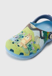 Zoccoli in gomma colorati con design verde e blu, personaggi dei cartoni animati, fori di ventilazione, cinturino sul tallone e motivi texturizzati sulla superficie.