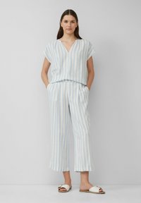 Leichtes, gestreiftes Pyjama-Set in Blau und Weiß. Kurzärmeliges Oberteil mit V-Ausschnitt; weite, gekürzte Hosen; kombiniert mit weißen Sandalen.
