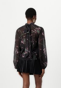 Blusa nera floreale con maniche lunghe e puff. Caratterizzata da un tessuto trasparente con motivi di fiori viola e verdi.