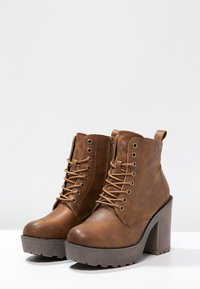 Brązowe botki na obcasie sięgające kostki, wykonane z ekologicznej skóry, z przodem na sznurówki, bocznym zamkiem błyskawicznym oraz teksturowaną podeszwą platformową z bieżnikiem.