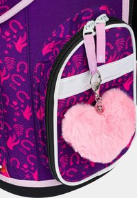 Zaino viola con accenti rosa e bianchi, caratterizzato da un design della tasca a motivo, hardware argentato e un portachiavi a forma di cuore fluffy rosa.