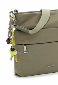 Torebka w oliwkowej zieleni, wodoodporna, o gładkiej fakturze, wyposażona w odpinany pasek, kieszeń na zamek oraz ozdobne breloczki. Logo widoczne.