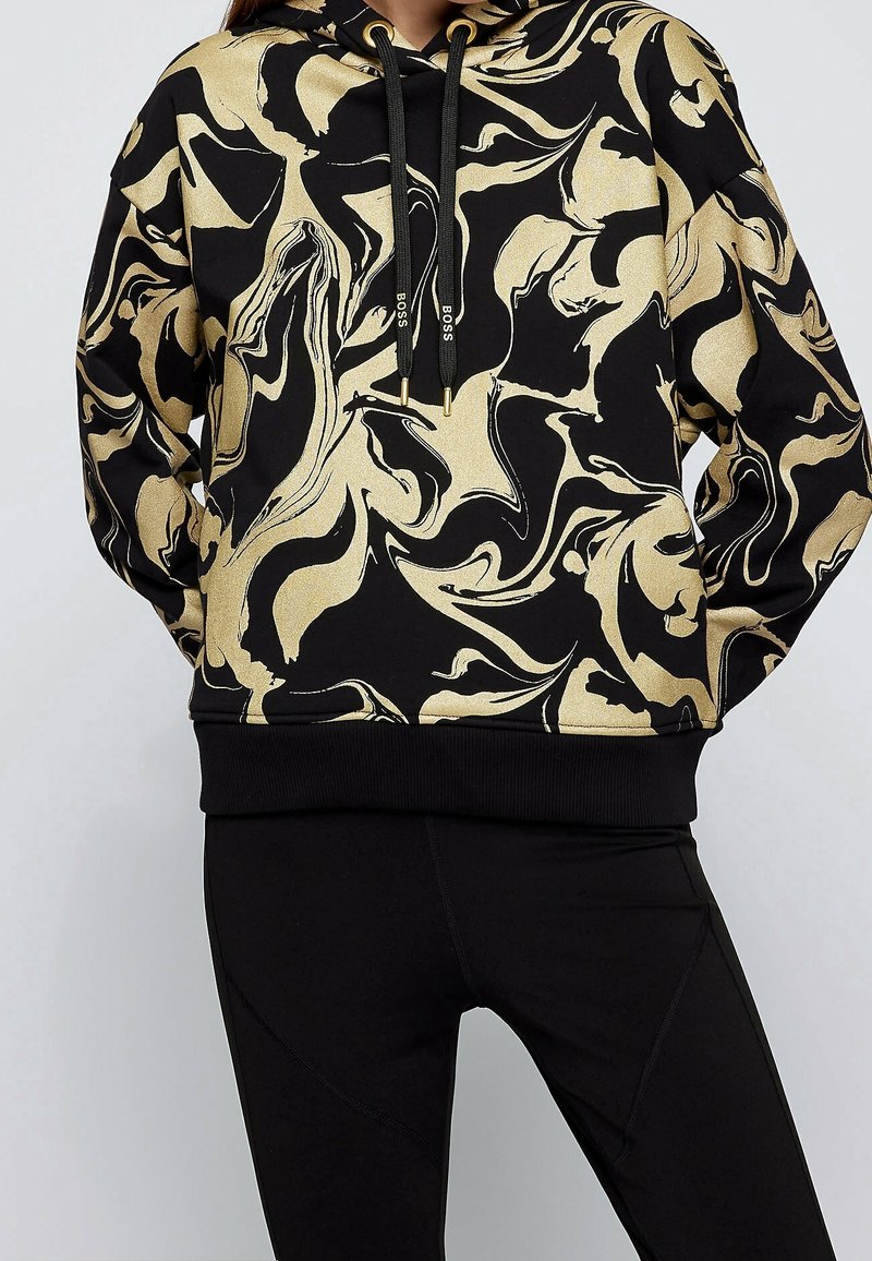 Sudadera con capucha en negro con un patrón abstracto de remolinos dorados, que incluye un bolsillo canguro y cordones con acentos dorados.
