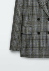 Blazer gris croisé avec motif à carreaux bleu et noir, boutons noirs et poche à rabat sur le côté gauche.