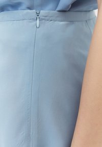 Robe bleu clair montrant un gros plan d'une fermeture éclair latérale et des détails de couture, avec une texture de tissu lisse et légèrement brillante.