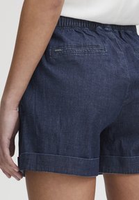 Tumši indigo krāsas d�žinsu šorti ar elastīgu jostu, aizmugurējām kabatām un salocītu maliņu. Gluda tekstūra ar minimālu apdari.