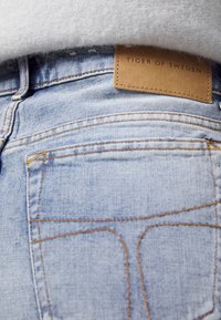 Světle modré džínové kalhoty s béžovou koženou etiketou s nápisem "TIGER OF SWEDEN." Viditelné význačné švy a design zadní kapsy.