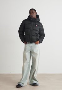 Black puffer jacket with a hood, featuring a logo patch; paired with light blue wide-leg jeans and black slip-on shoes.