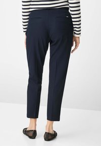 Marineblauwe nette broek met een slimfit, met een gladde textuur en twee achterzakken. Gecombineerd met zwarte slip-on schoenen van mesh.